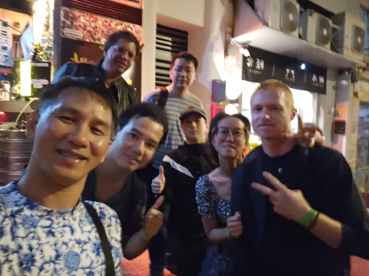 Eight PubSwap guests squeezed together for a group photo on a Lan Kwai Fong street outside a bar.