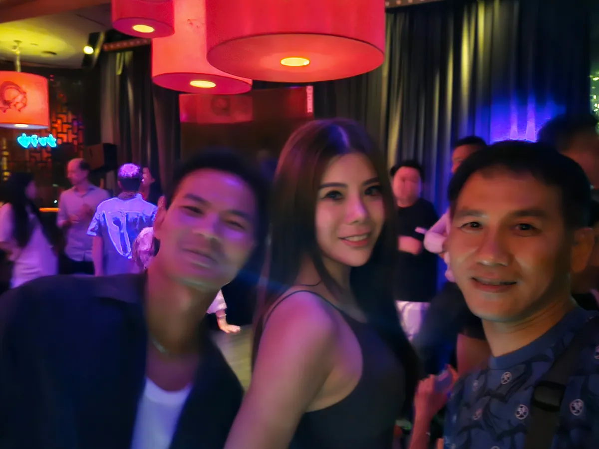 Three guests posing in a bar lit by red drum lampshades and purple wall lights.